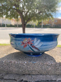 Decorative ceramic bowl with floral and dragonfly design on a concrete surface.